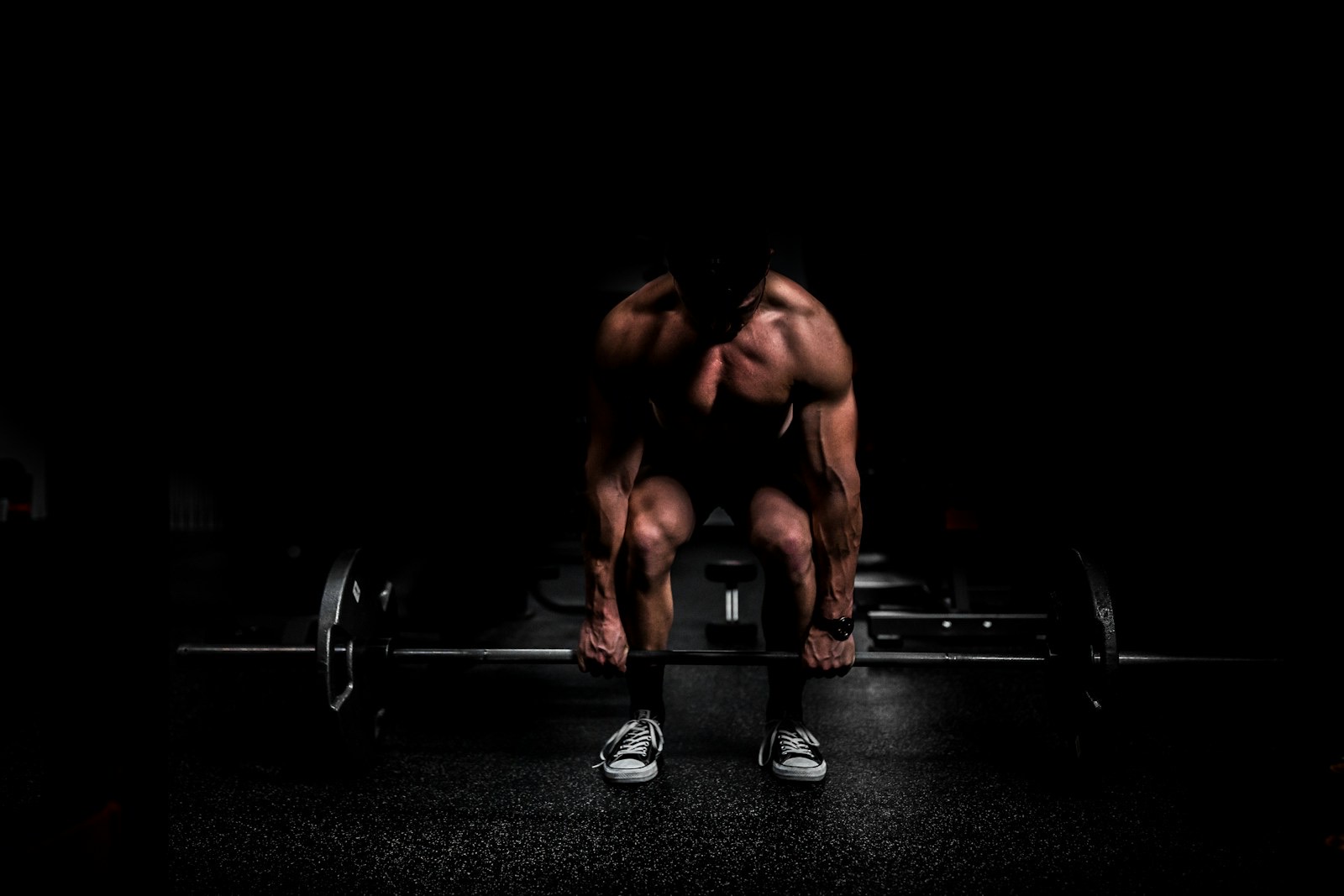 A lifter performing a barbell exercise in a gym with weights racked behind